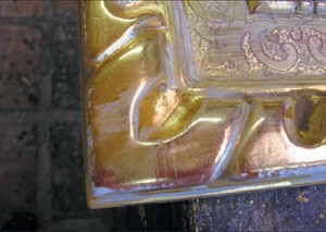 A close up shows the frame after the “rub,” when the gold has been abraded through the leaf, down to the clay, and into the gesso in certain areas with a pumice and alcohol mixture. 